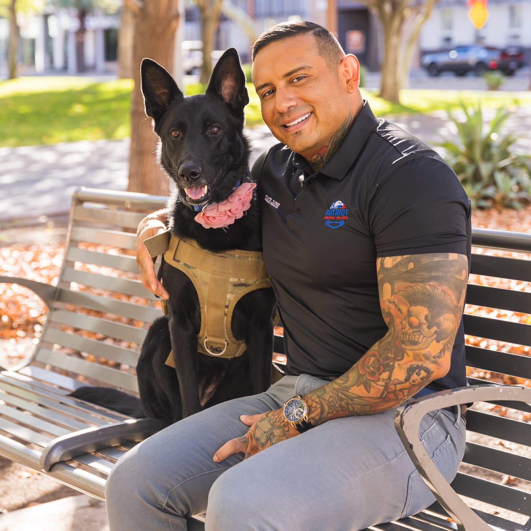 Jaime Martinez sitting on a park bench with a black shepherd wearing a pink flower collar